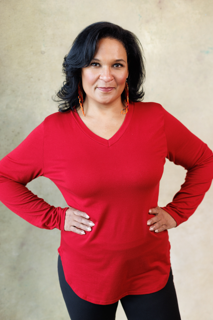 Maya in a red top, hands on hips
