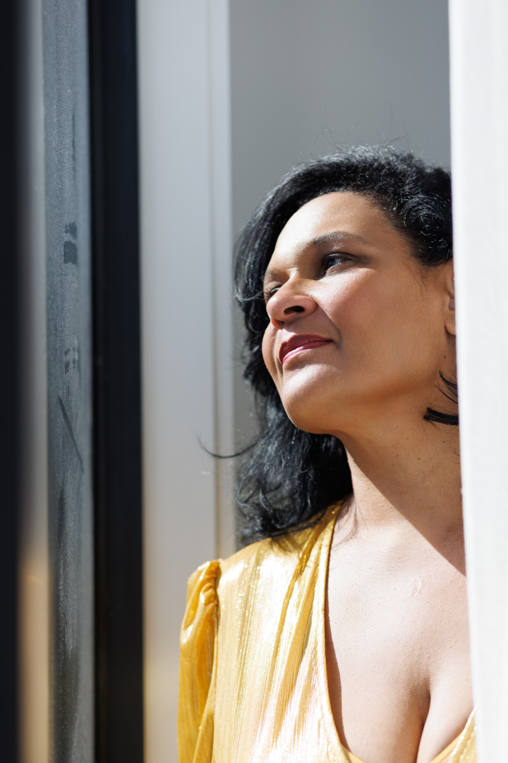Maya in gold, looking out a window into sunlight